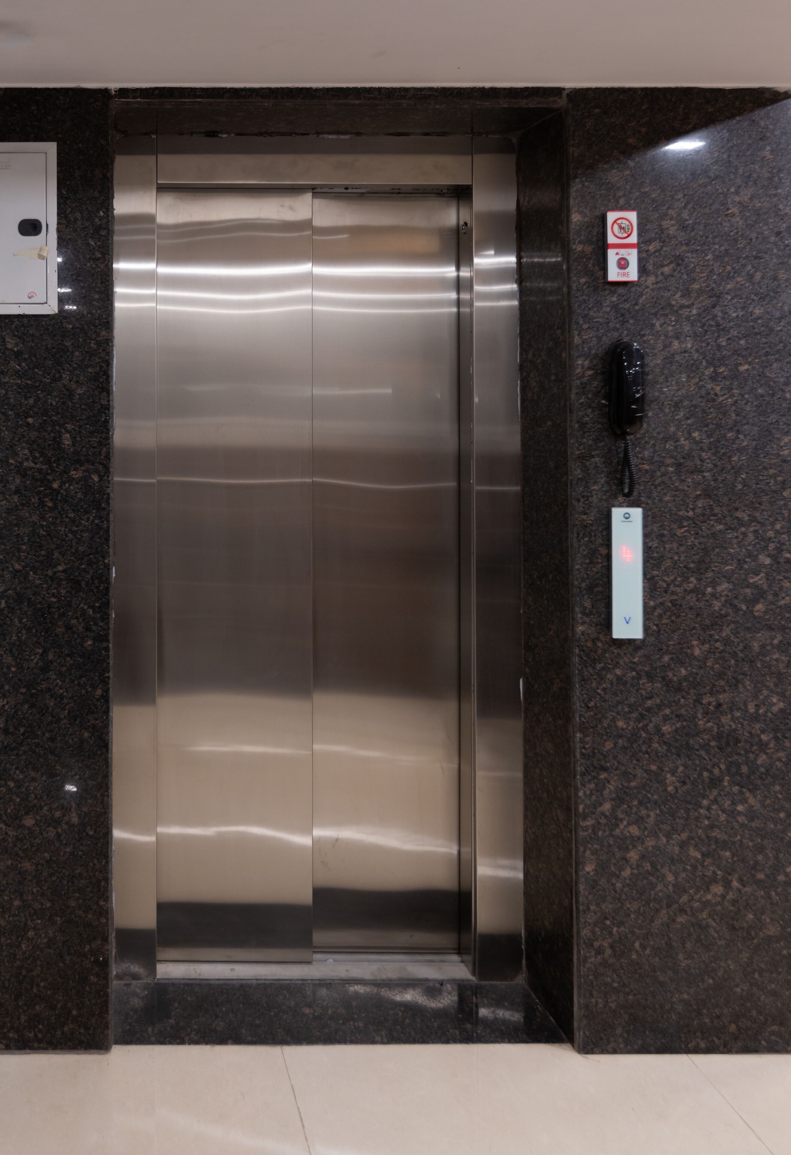 An elevator with a metallic finish, a wall-mounted intercom, and a no-smoking sign.