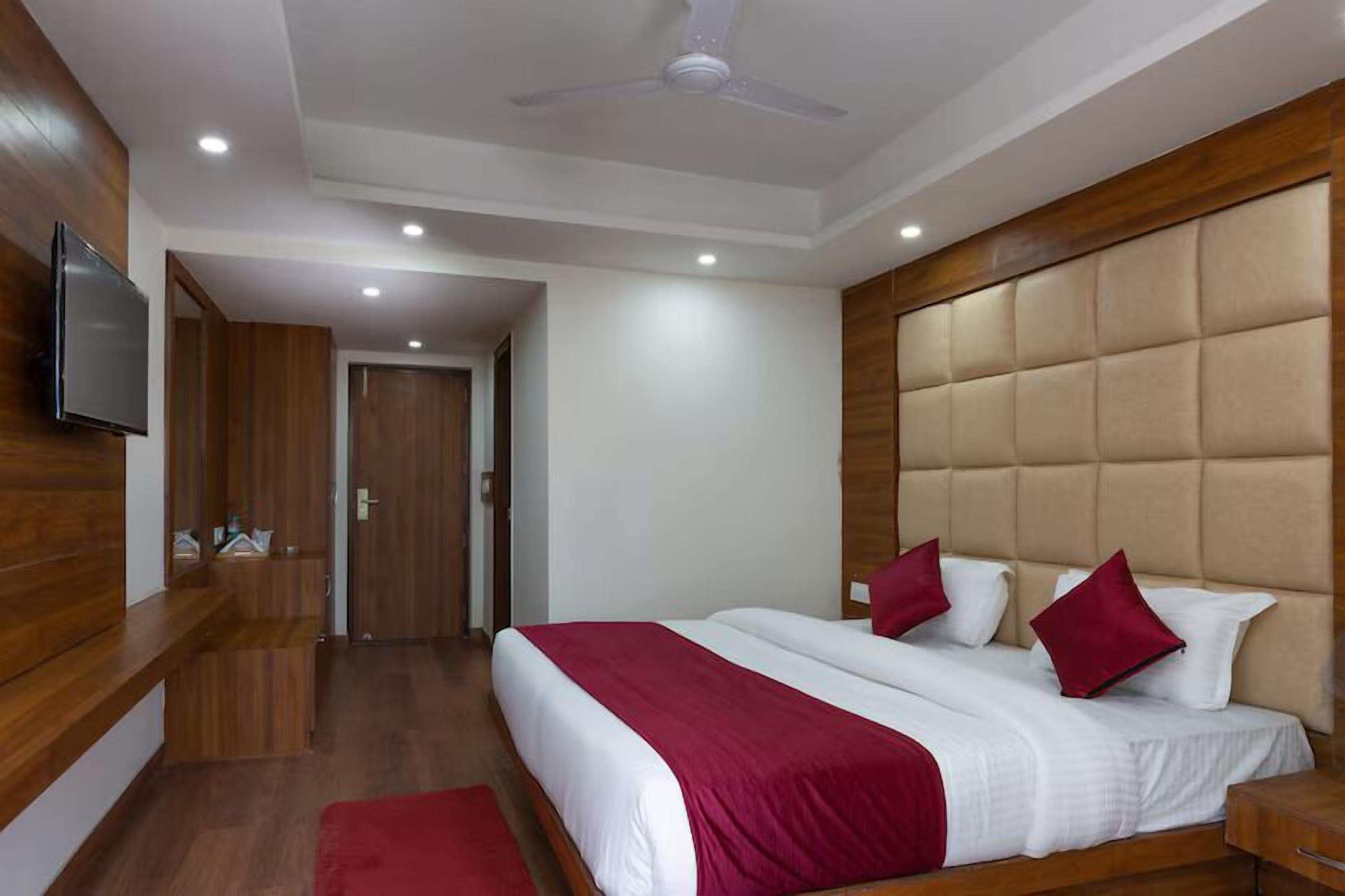 Una habitación de hotel con una cama grande, un cabecero de madera, un televisor montado en la pared y un ventilador de techo.
