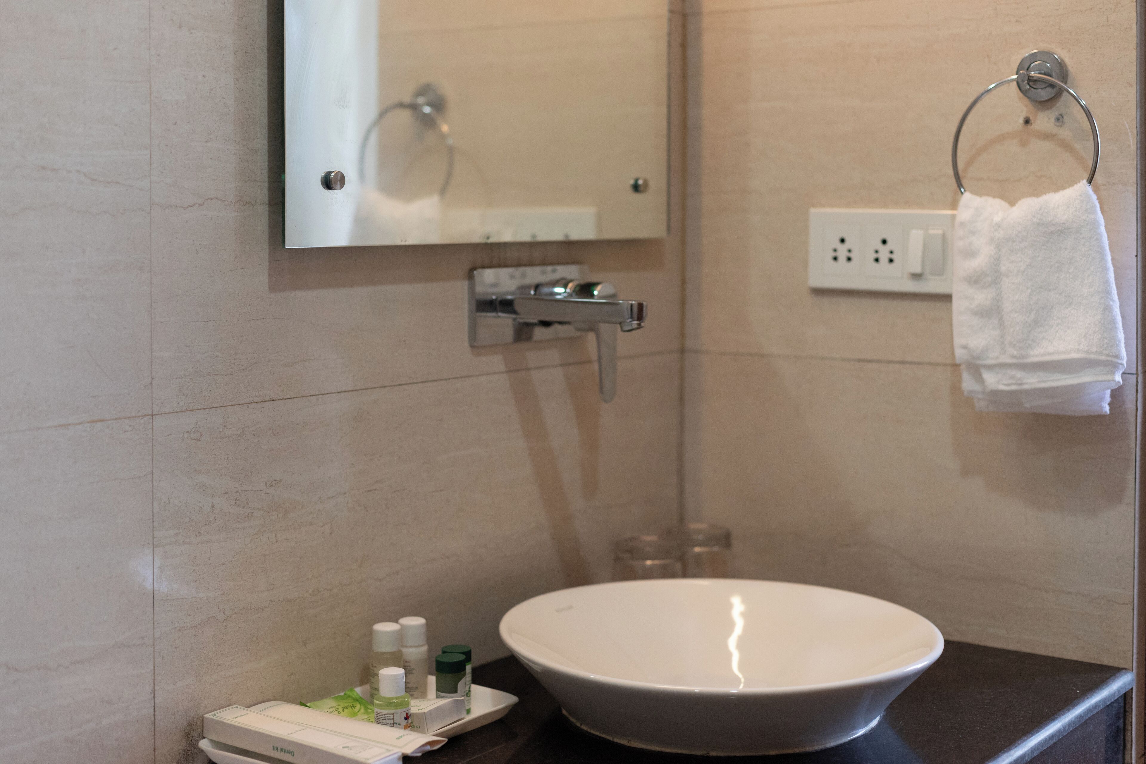 A bathroom with a white sink, a mirror, a towel ring, and a small shelf with toiletries.