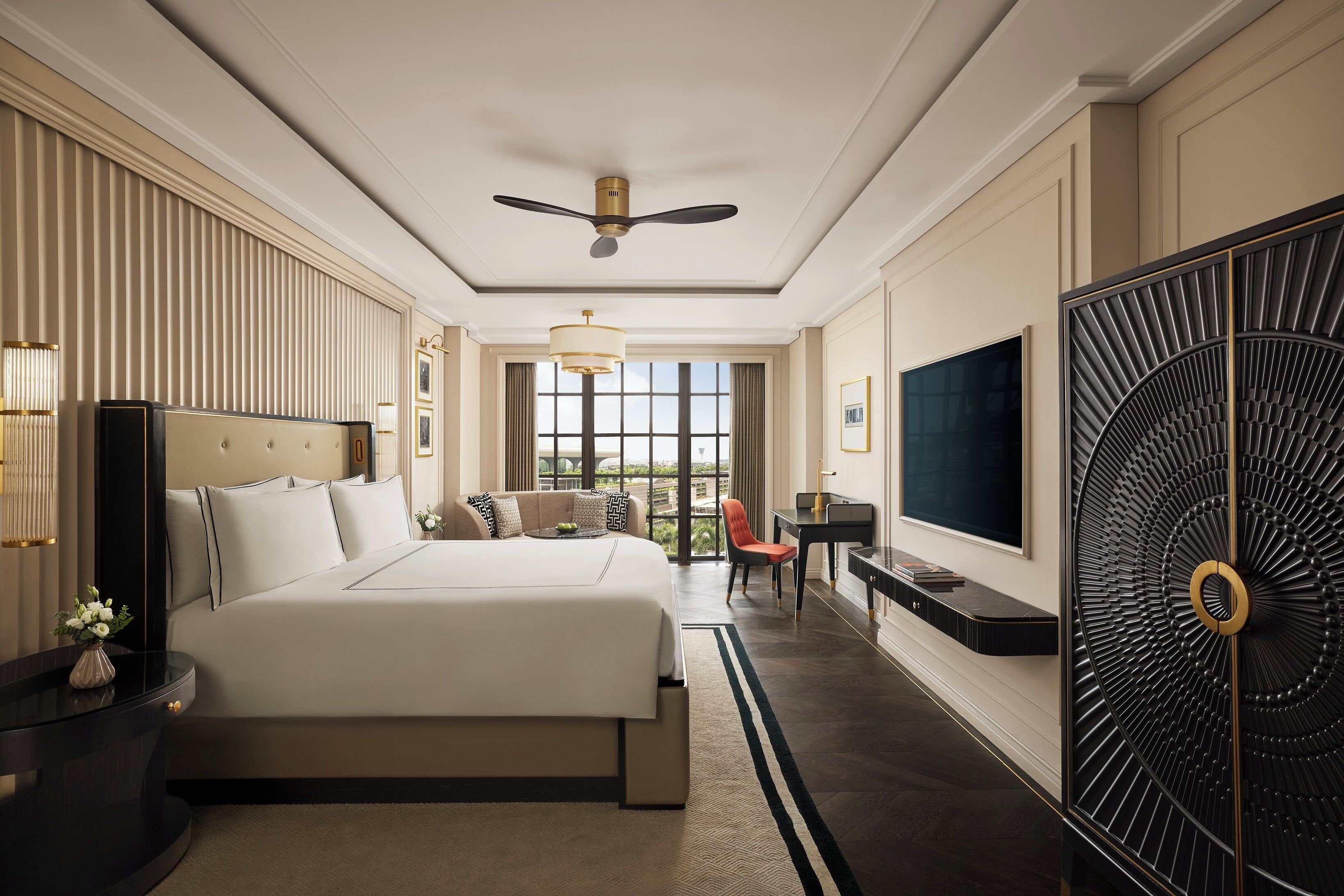 A hotel room with a large bed, a desk, a TV, and a balcony with a view.