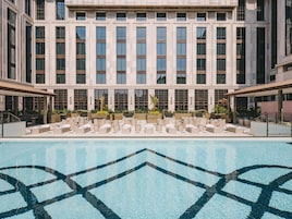 Un hotel con una piscina grande, zona de estar al aire libre y una fachada de edificio moderna.
