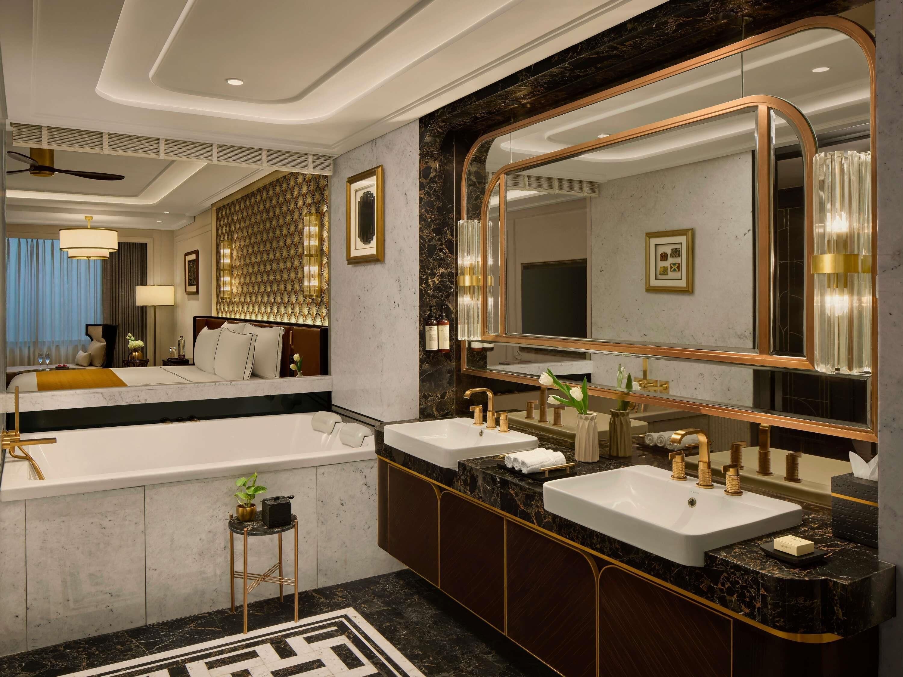 Un baño de hotel moderno con un espejo grande, dos lavamanos, una bañera y un tocador con encimera de mármol.