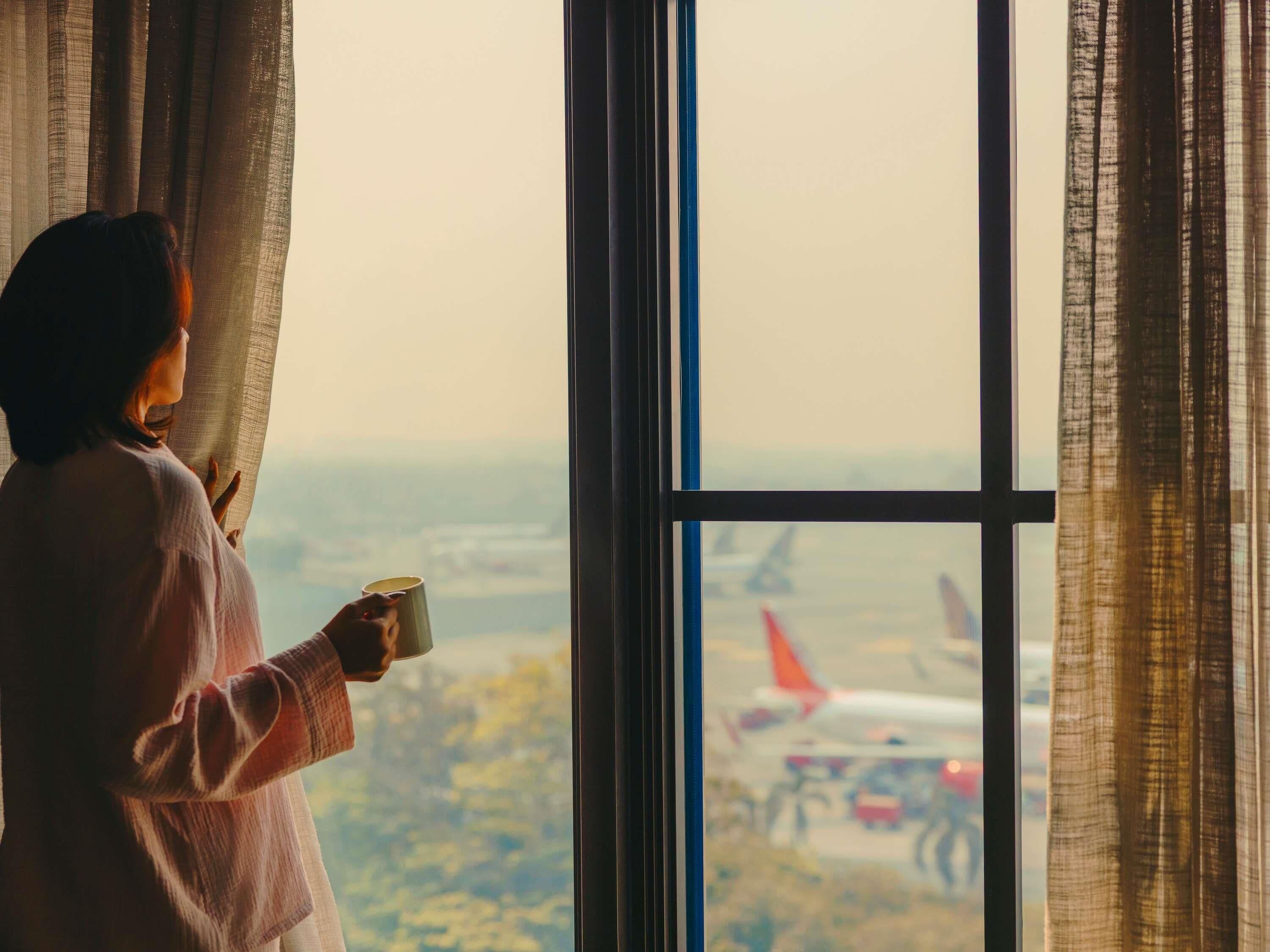 A person holding a cup by a window with a view of an airport.