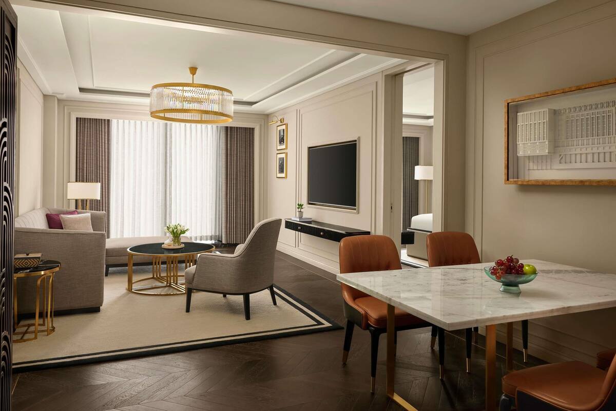 Quarto de hotel com área de jantar, sofá, televisão e lustre.