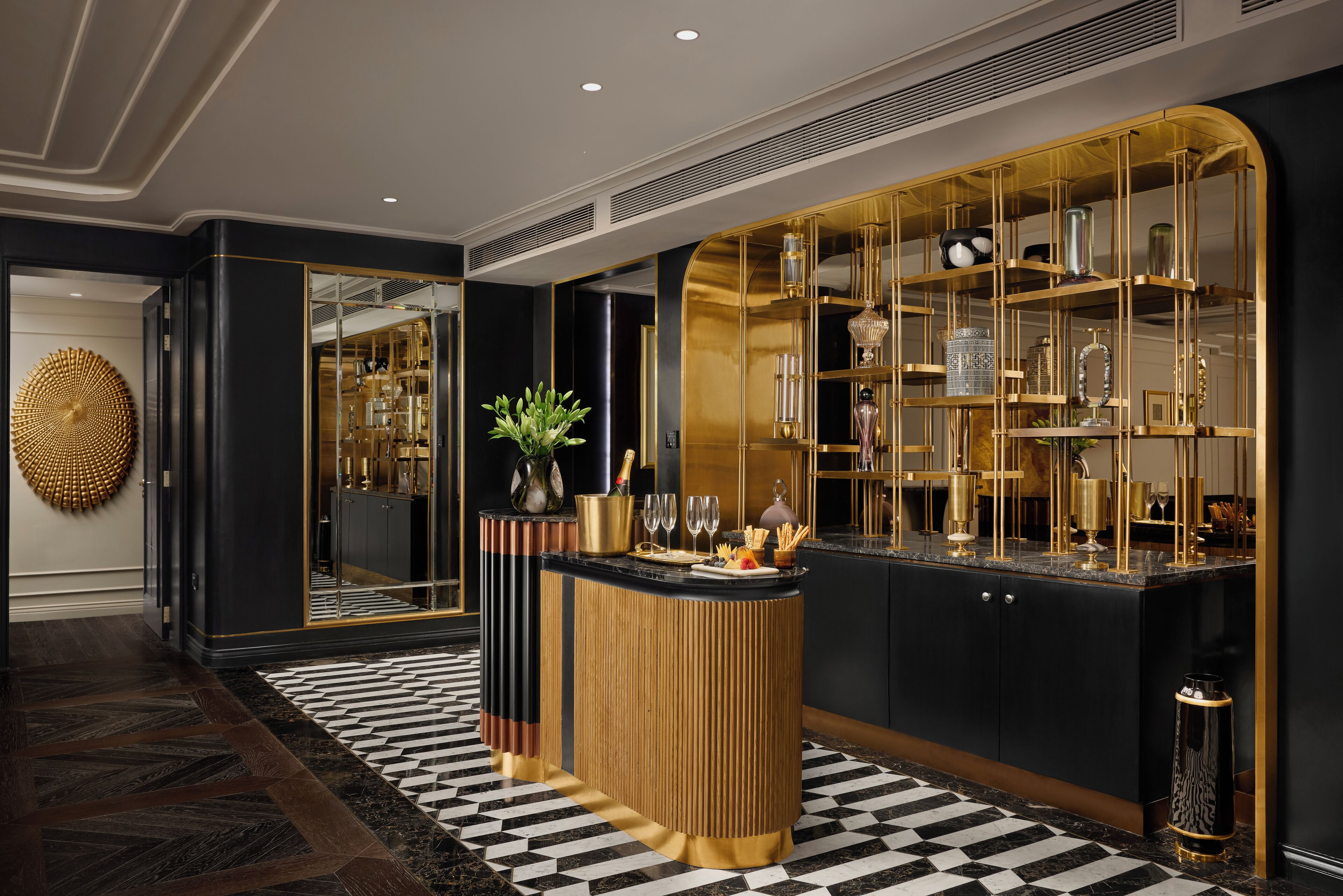 A modern bar area with a black and gold color scheme, featuring a central bar counter, a mirrored wall, and a decorative plant.