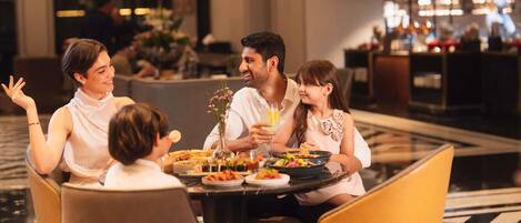 Una familia cenando en el restaurante de un hotel, con un bar al fondo.