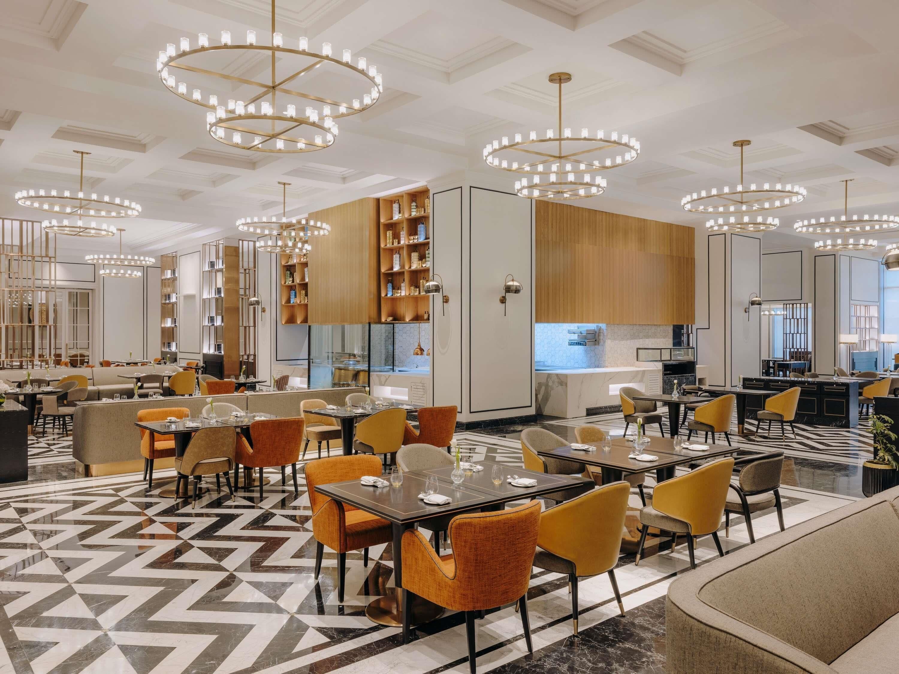 A modern restaurant with multiple dining areas, round chandeliers, and a geometric patterned floor.