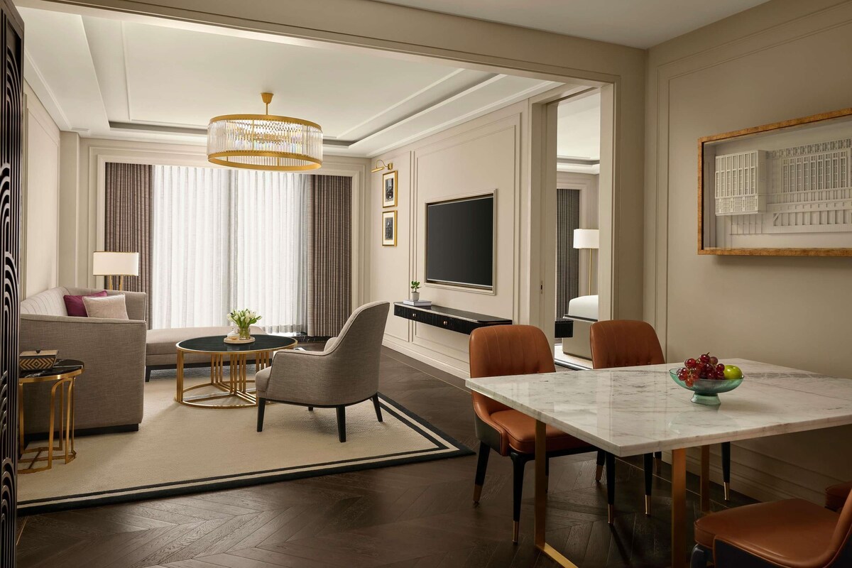 A hotel room with a dining area, a sofa, a TV, and a chandelier.