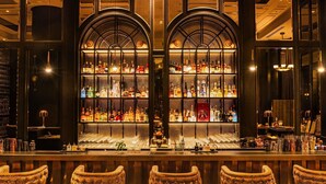 Un bar con una amplia exhibición de botellas de licor, una barra y cuatro taburetes tapizados.