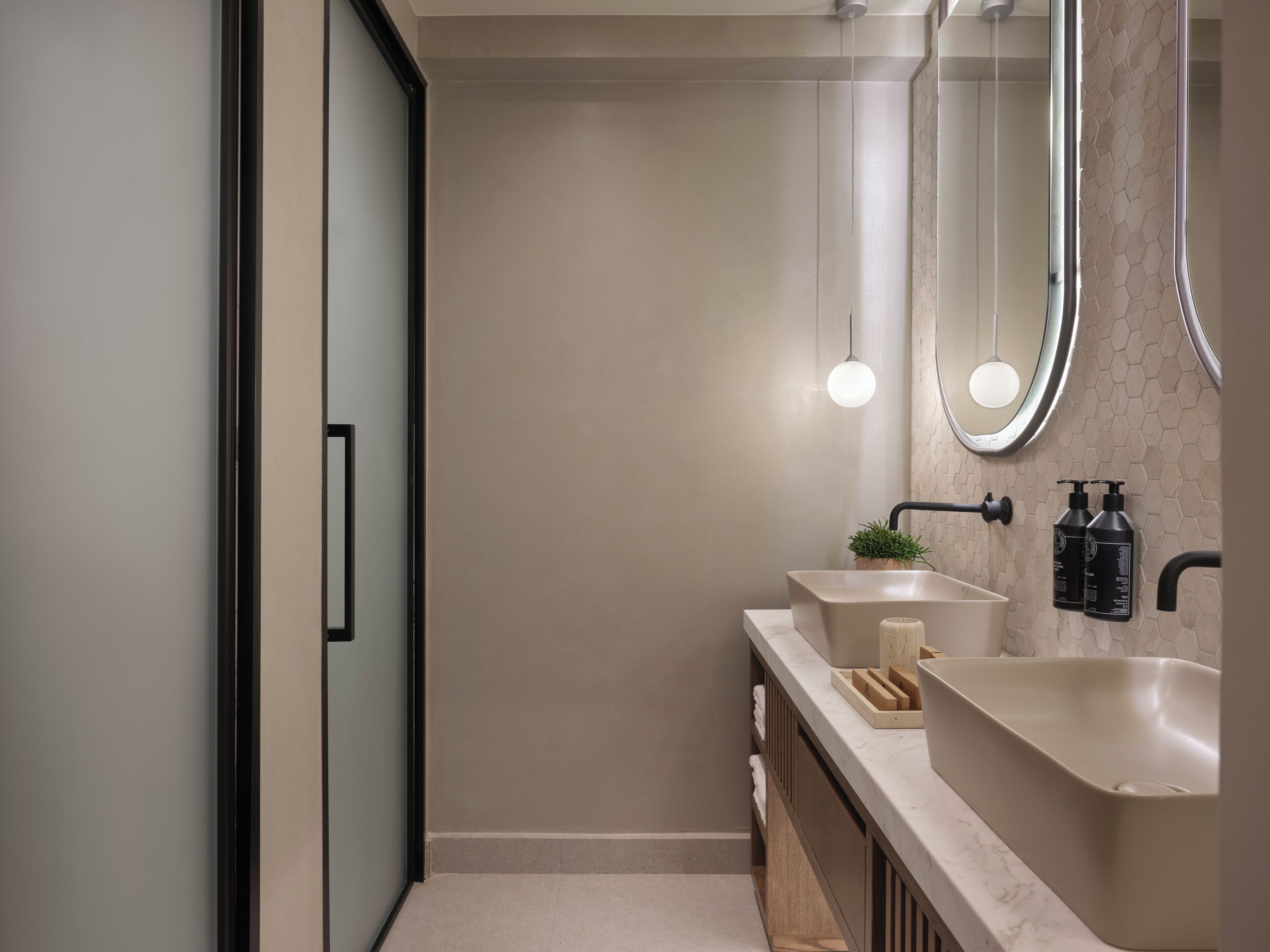 A modern bathroom with a large mirror, two sinks, and a shower area.