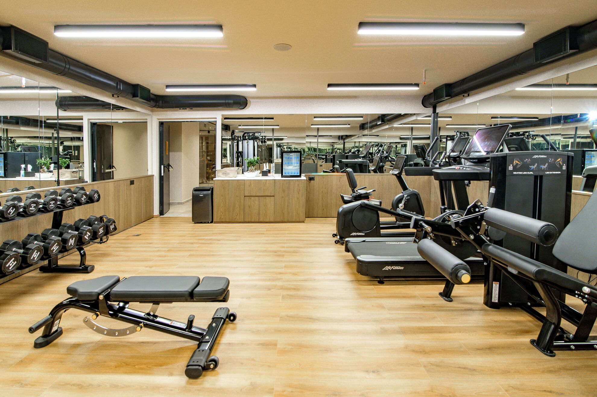 Un gimnasio con equipo de ejercicio, espejos y suelo de madera.