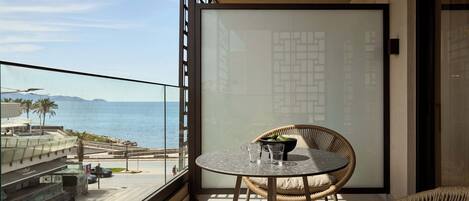 A balcony with a round table and wicker chairs, overlooking a beach and the sea.