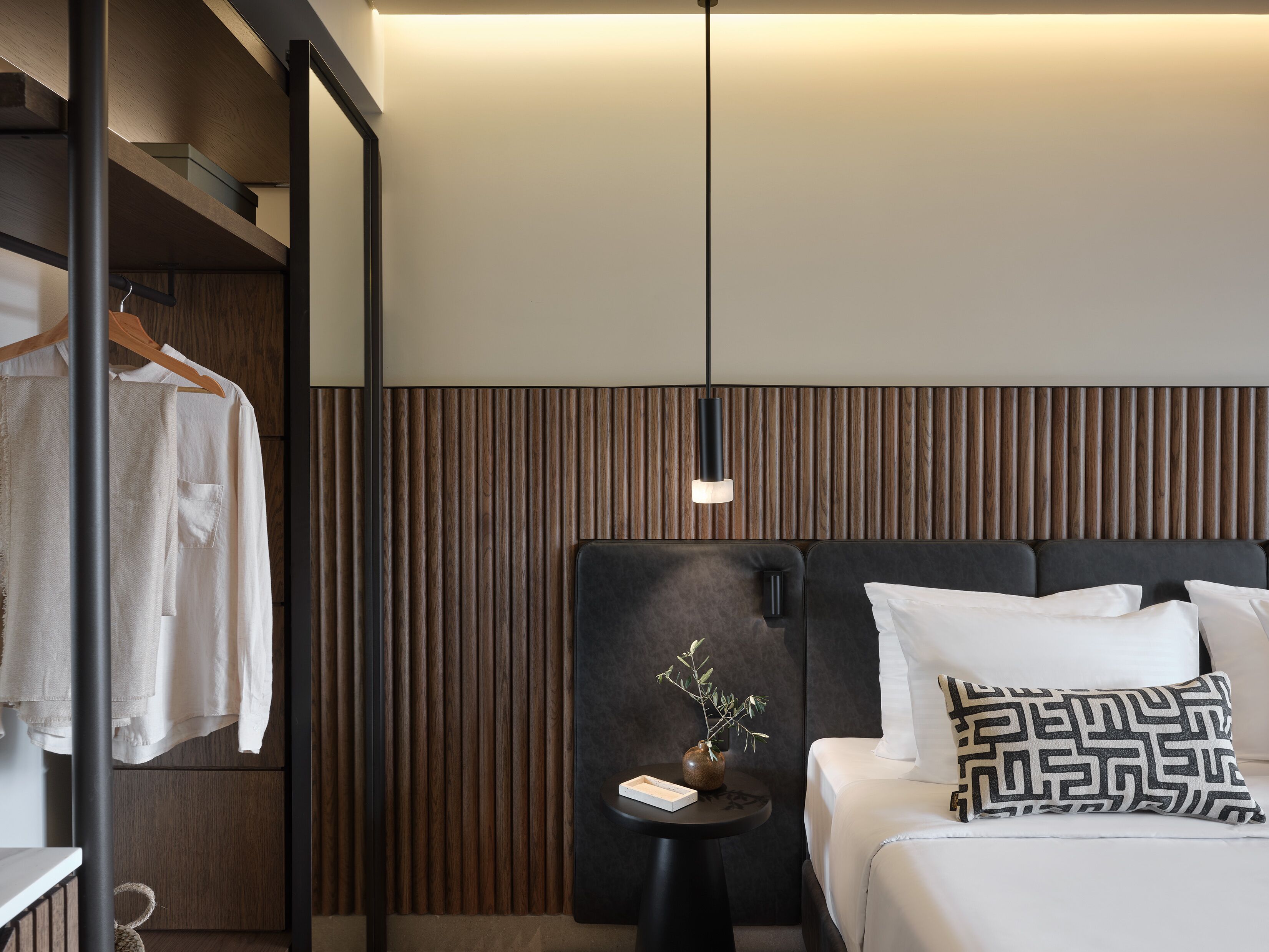 A modern hotel room with a bed, bedside table, and a mirror.