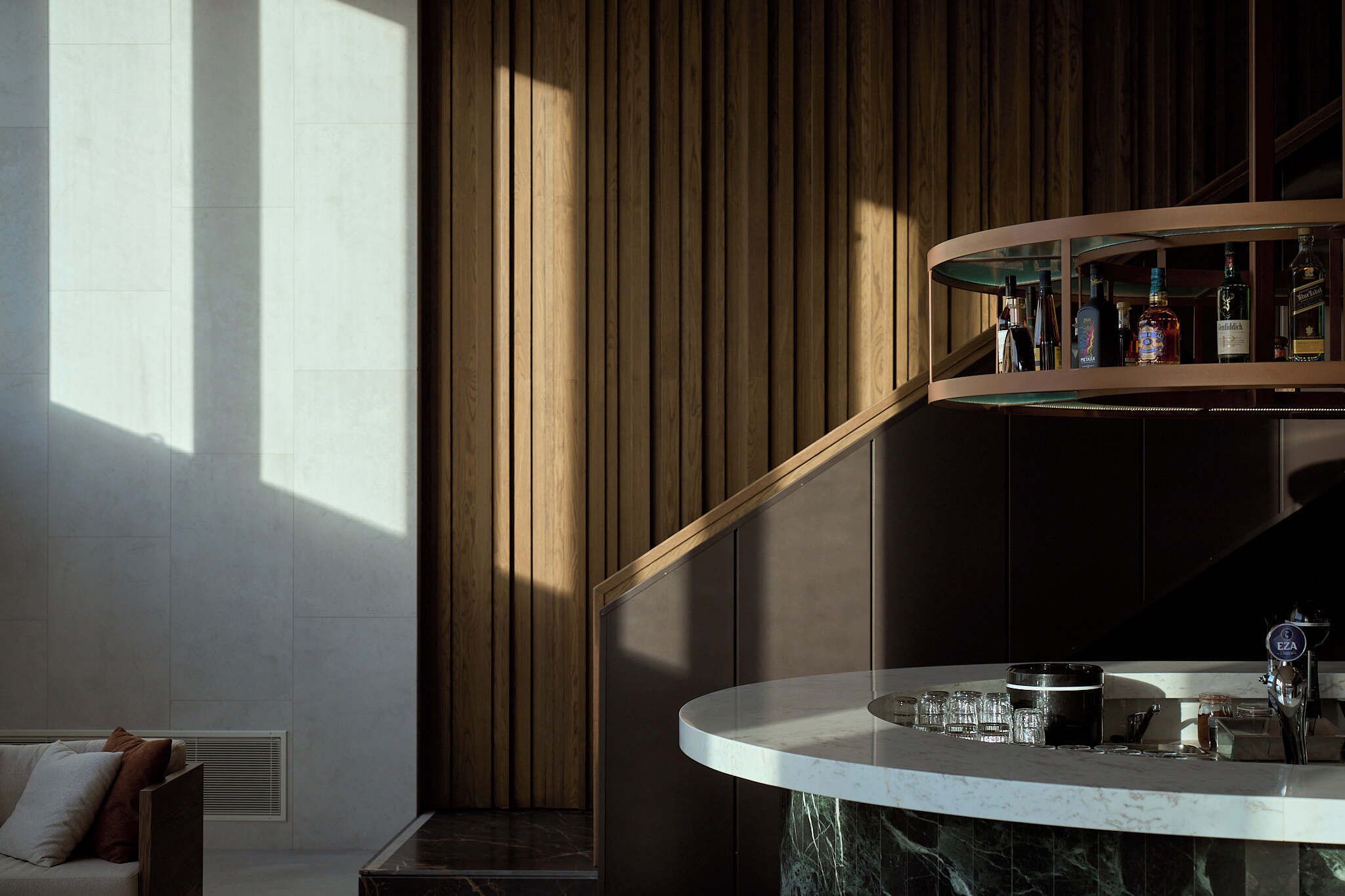 A modern bar area with a curved countertop, a selection of bottles, and a faucet.