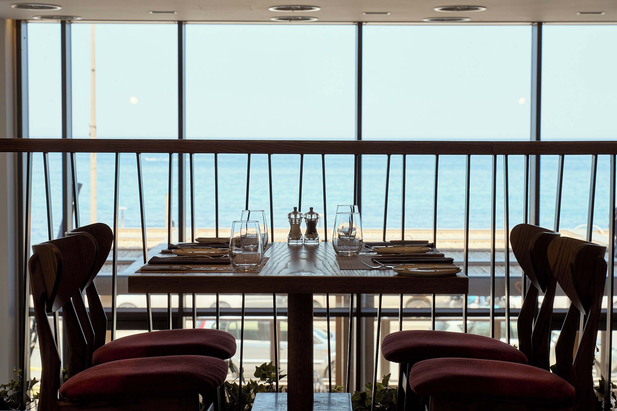 A dining area with a view of the beach, featuring a wooden table set for two with chairs.