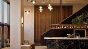 A modern bar area with a marble countertop, wooden accents, and hanging pendant lights.