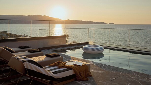 An infinity pool with lounge chairs and a view of the sea at sunset.