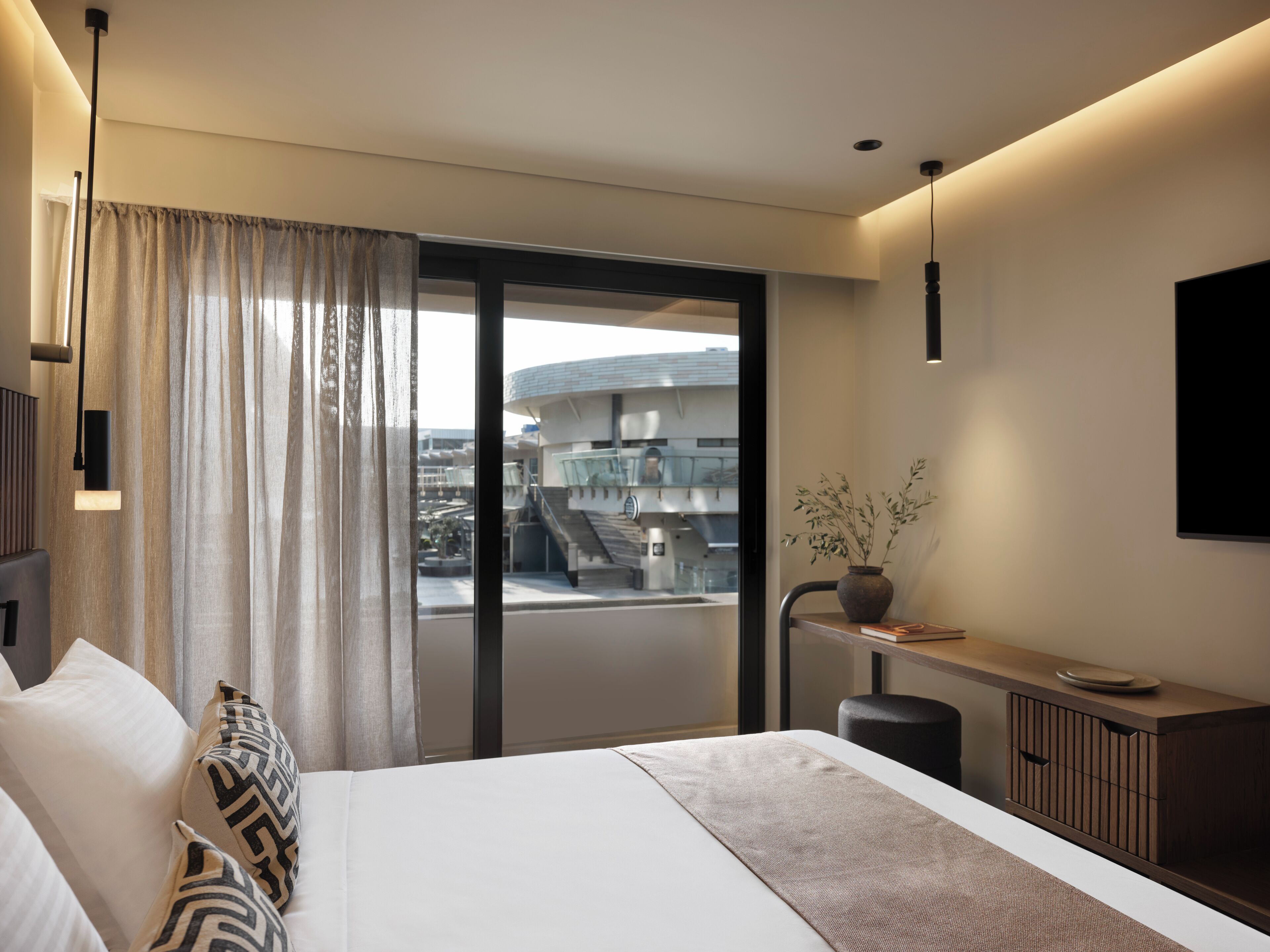 A modern hotel room with a large bed, a view of the city, and a balcony with a glass railing.