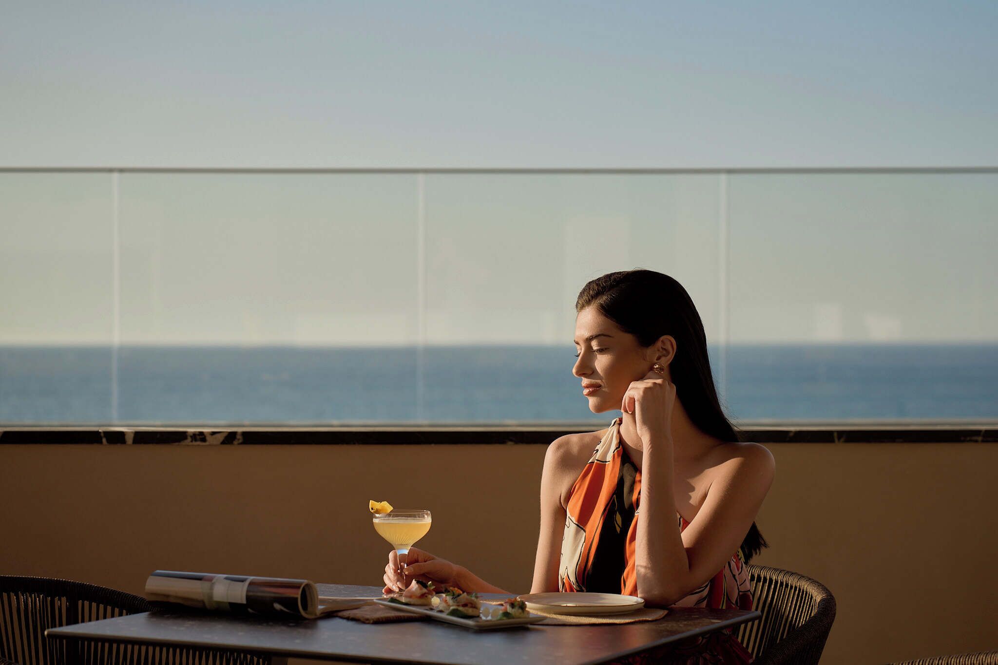 Une personne est assise à une table, devant un verre et un menu, et elle jouit d’une vue sur l’océan.
