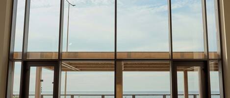 Amplia habitación con grandes ventanales con vistas a una playa y al mar. Hay varias sillas y un sofá para sentarse.
