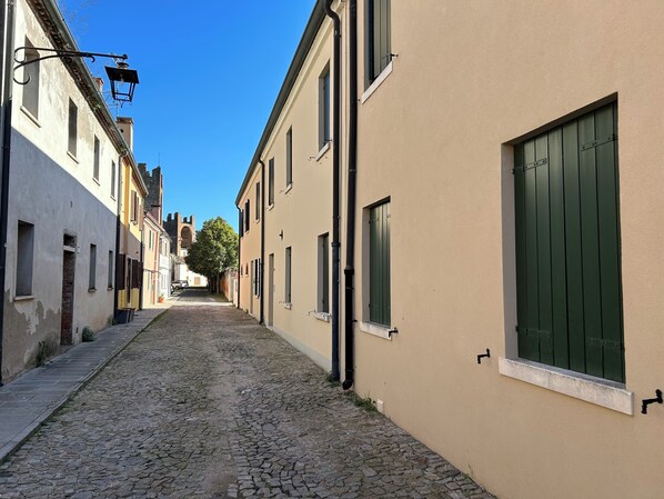 A narrow cobblestone street flanked by buildings with shutters and a street lamp.