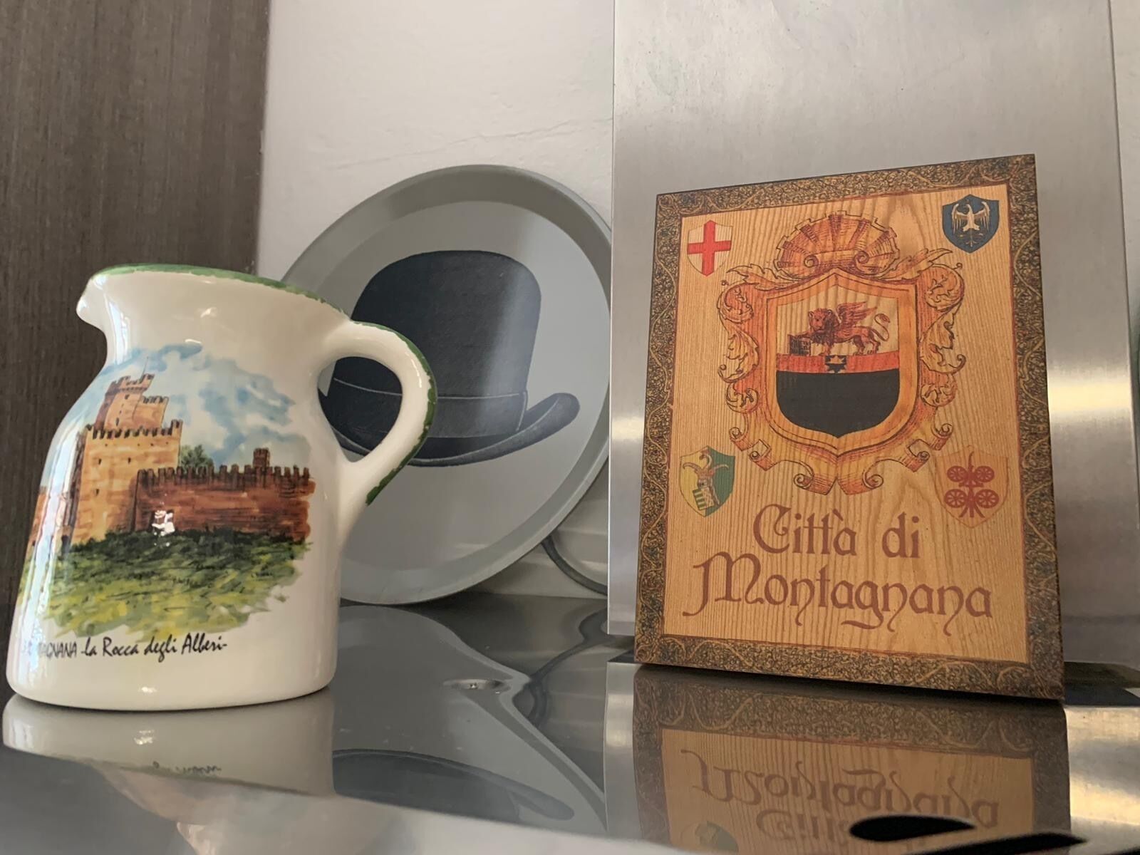 Een keramieken pitcher met een kasteelafbeelding, een houten plaquette met een familiewapen en een zwarte hoed.