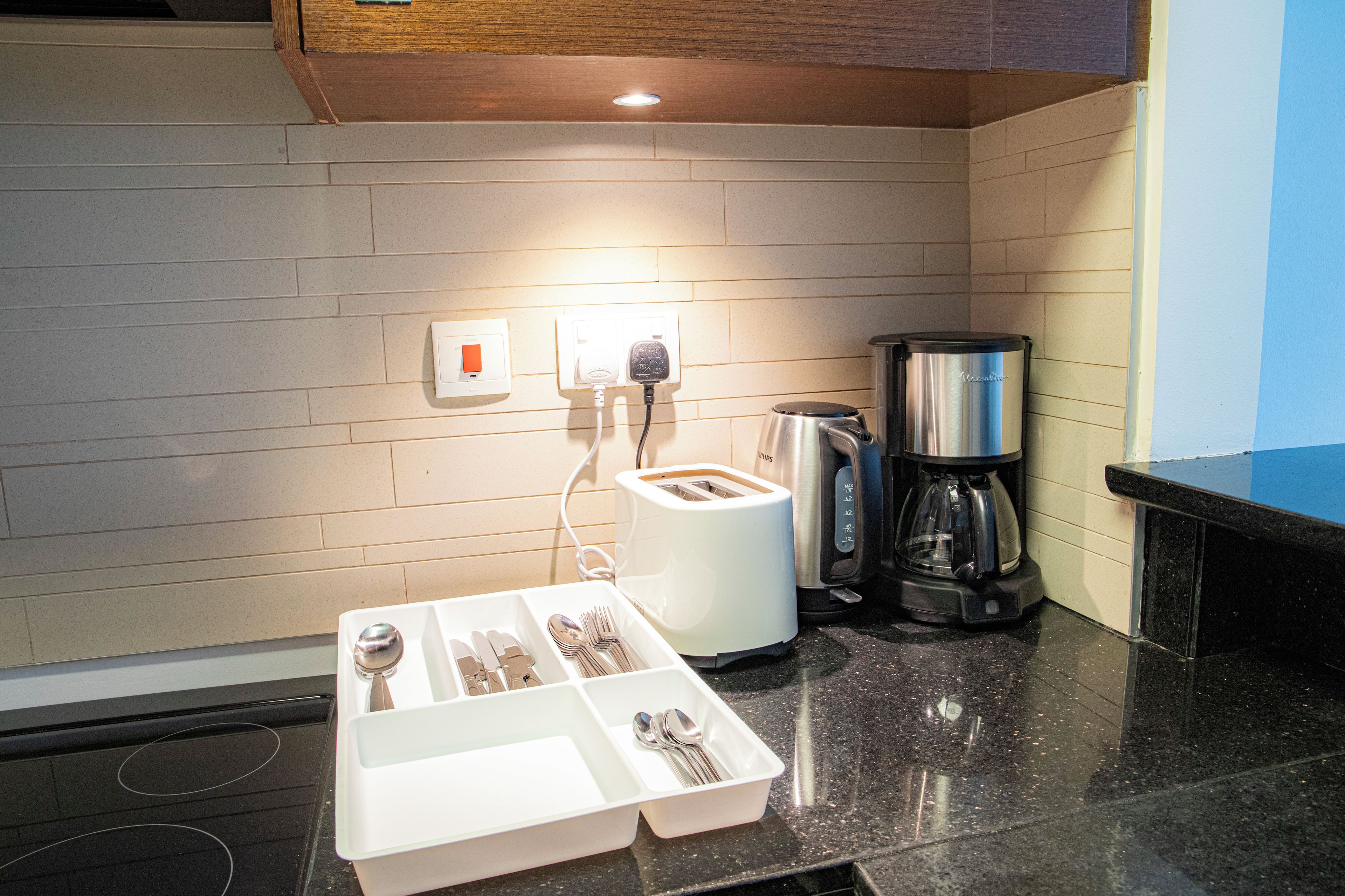 Een kitchenette met een broodrooster, koffiezetapparaat en een witte schaal met bestek.