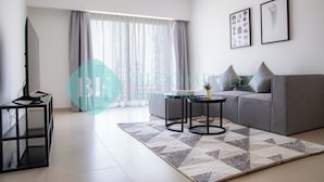 Una sala moderna con un sofá gris, dos mesas de centro negras, un televisor sobre un mueble bajo y una alfombra estampada.