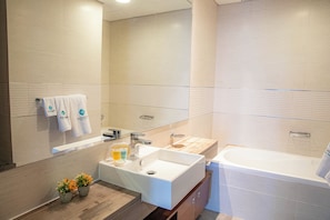 A modern bathroom with a large mirror, a sink, a bathtub, and a vanity with a mirror. There are towels hanging on the wall and a small plant on the vanity.