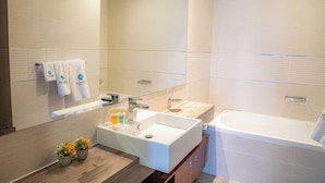 Un baño moderno con un lavamanos grande, una bañera y un espejo. Hay toallas colgadas en la pared y una planta pequeña en la encimera.