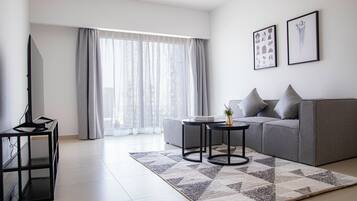 A modern living room with a grey sofa, two black side tables, a flat-screen TV, and a large window with sheer curtains.