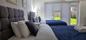 A bedroom with two beds, a large window, and a view of a green lawn. - House - Sleeps 7 - Parking - Station Close (Preston)