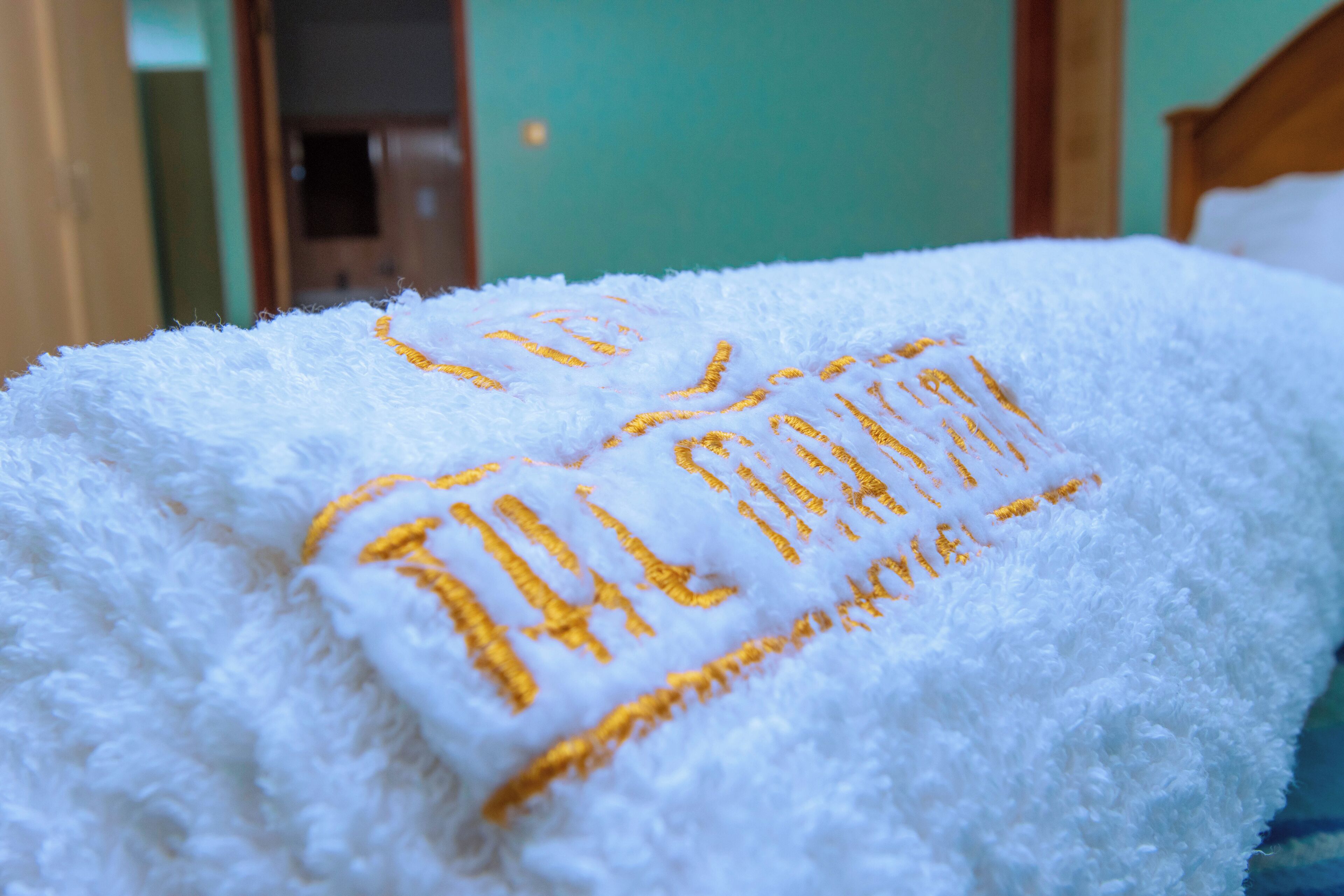 A white fluffy towel with embroidered text on a bed.