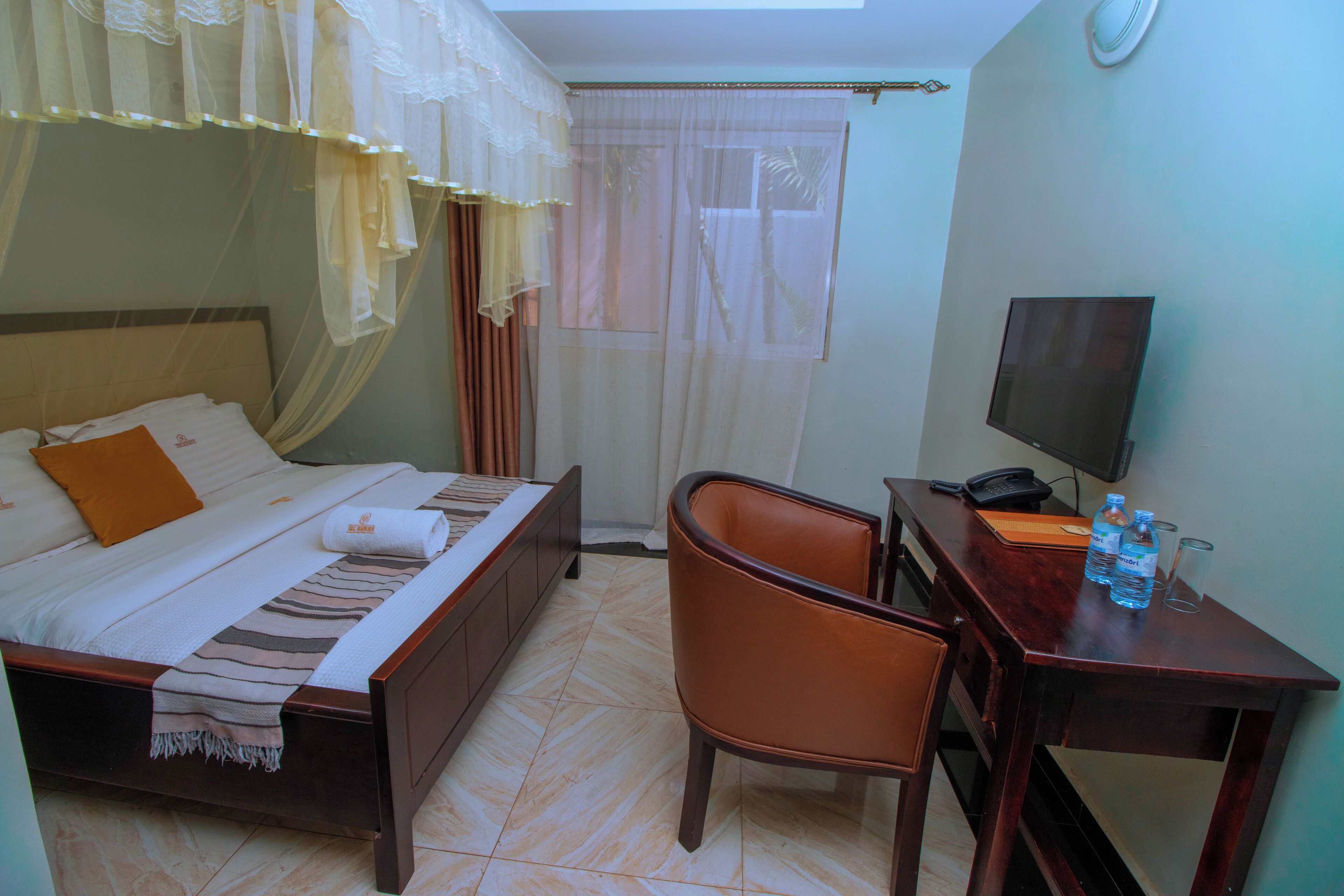 Habitación de hotel con cama, escritorio con silla, televisión y ventana con cortinas.