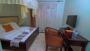 Habitación de hotel con cama, escritorio con silla, televisión y ventana con cortinas.