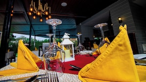 A dining table set with yellow napkins, clear glassware, and a red tablecloth. - The Mansion Hotel (Jinja)