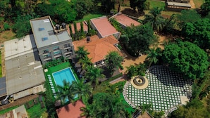 An aerial view of a hotel with multiple buildings, a swimming pool, and surrounding greenery. - The Mansion Hotel (Jinja)