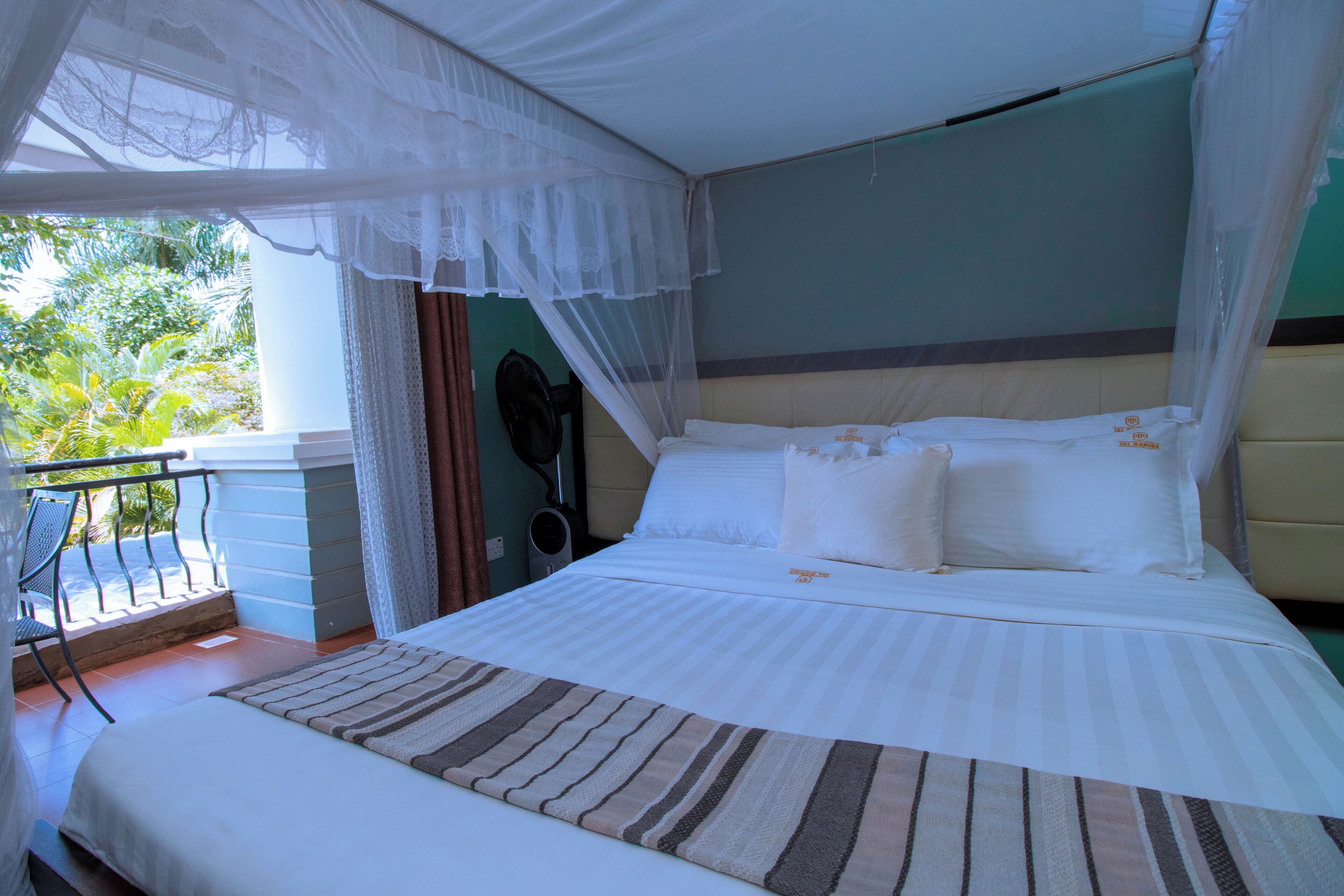 A bed with a canopy, a view of the outdoors, and a chair by the window.