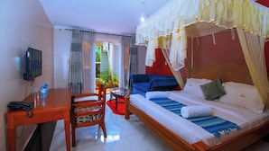 A hotel room with a bed, a desk, a chair, a TV, and a window with curtains. - The Mansion Hotel (Jinja)