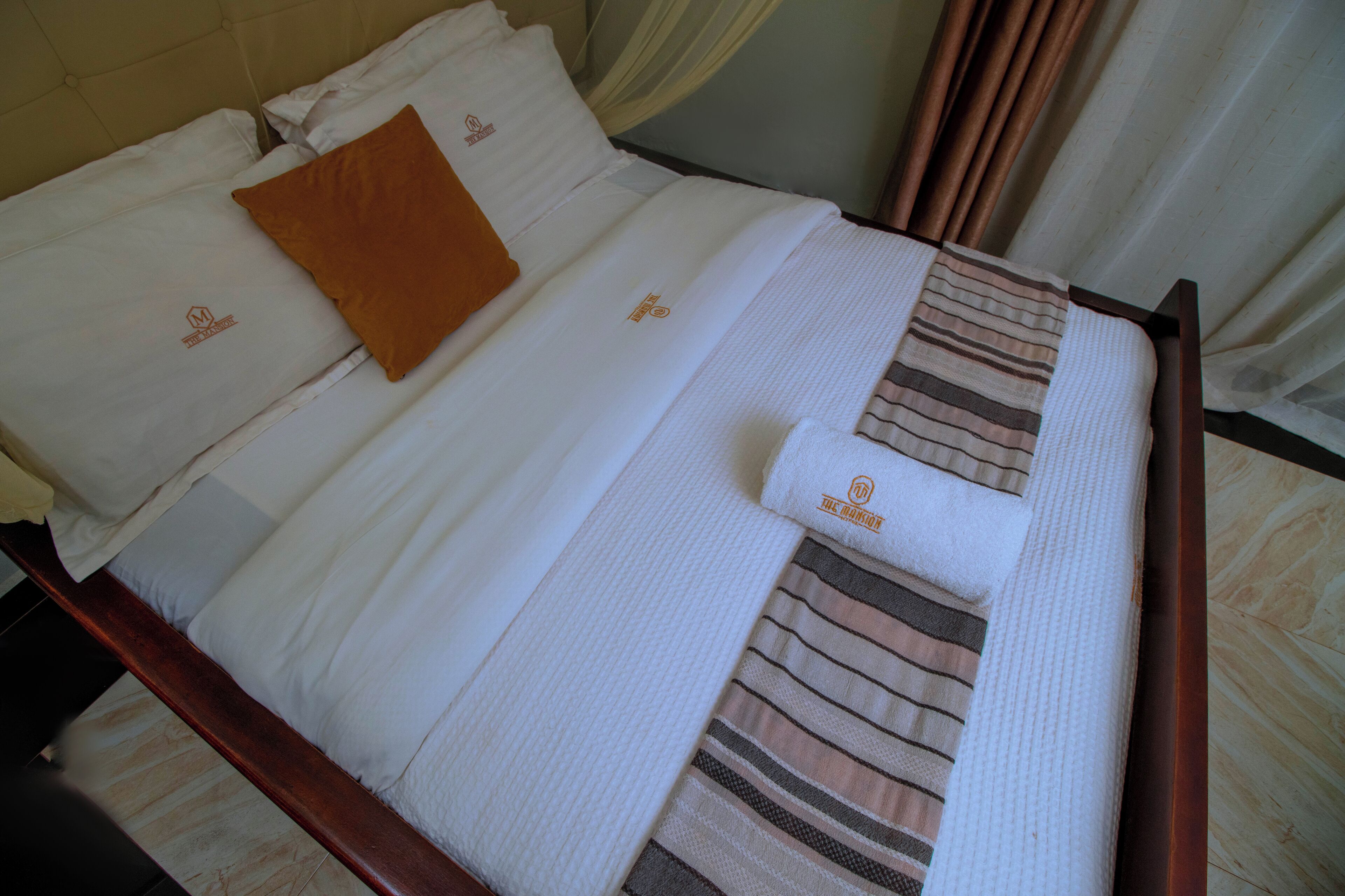 A neatly made bed with white linens, a brown pillow, and striped towels.