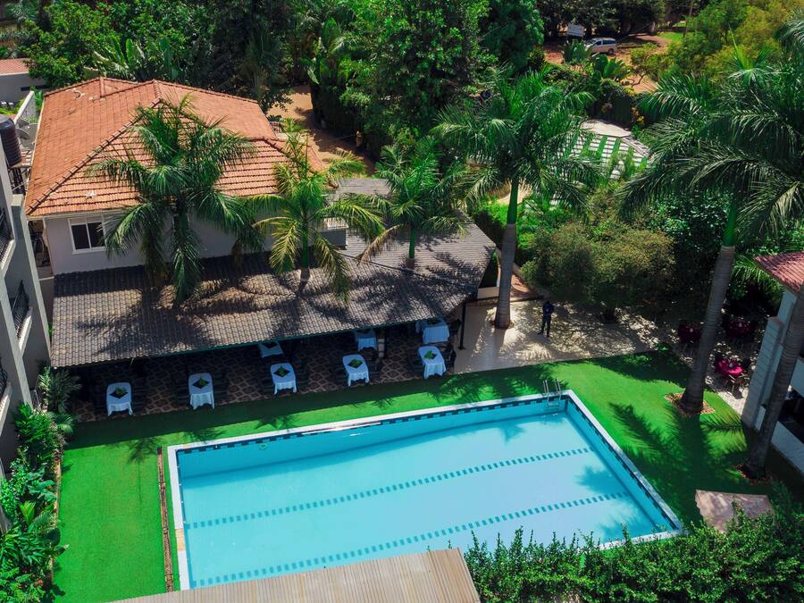 An aerial view of a hotel with a swimming pool, palm trees, and a tiled roof.