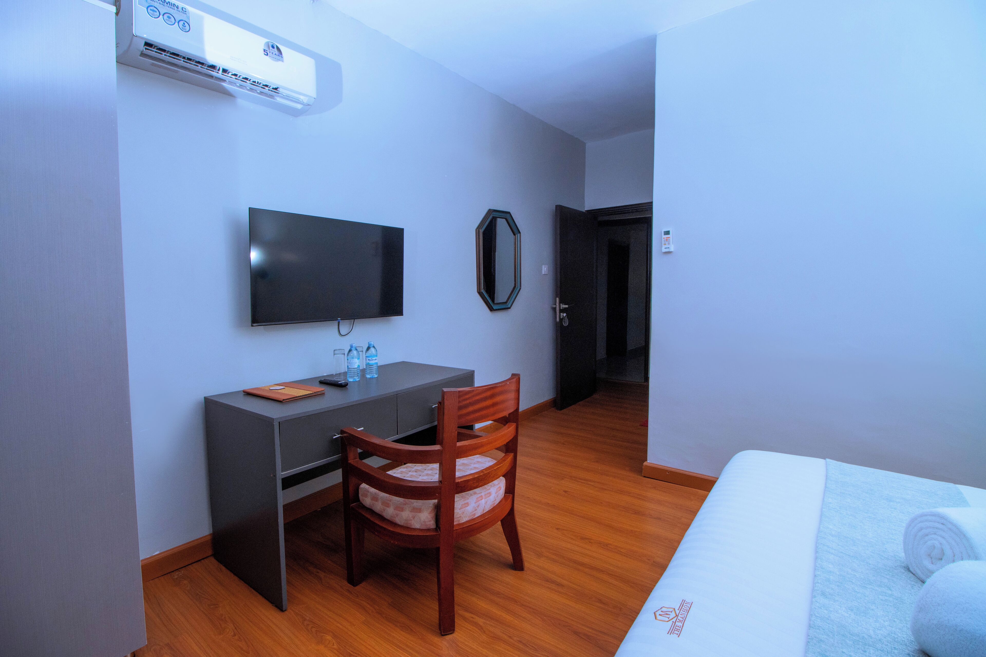 A hotel room with a bed, a desk with a chair, a television, and an air conditioning unit.
