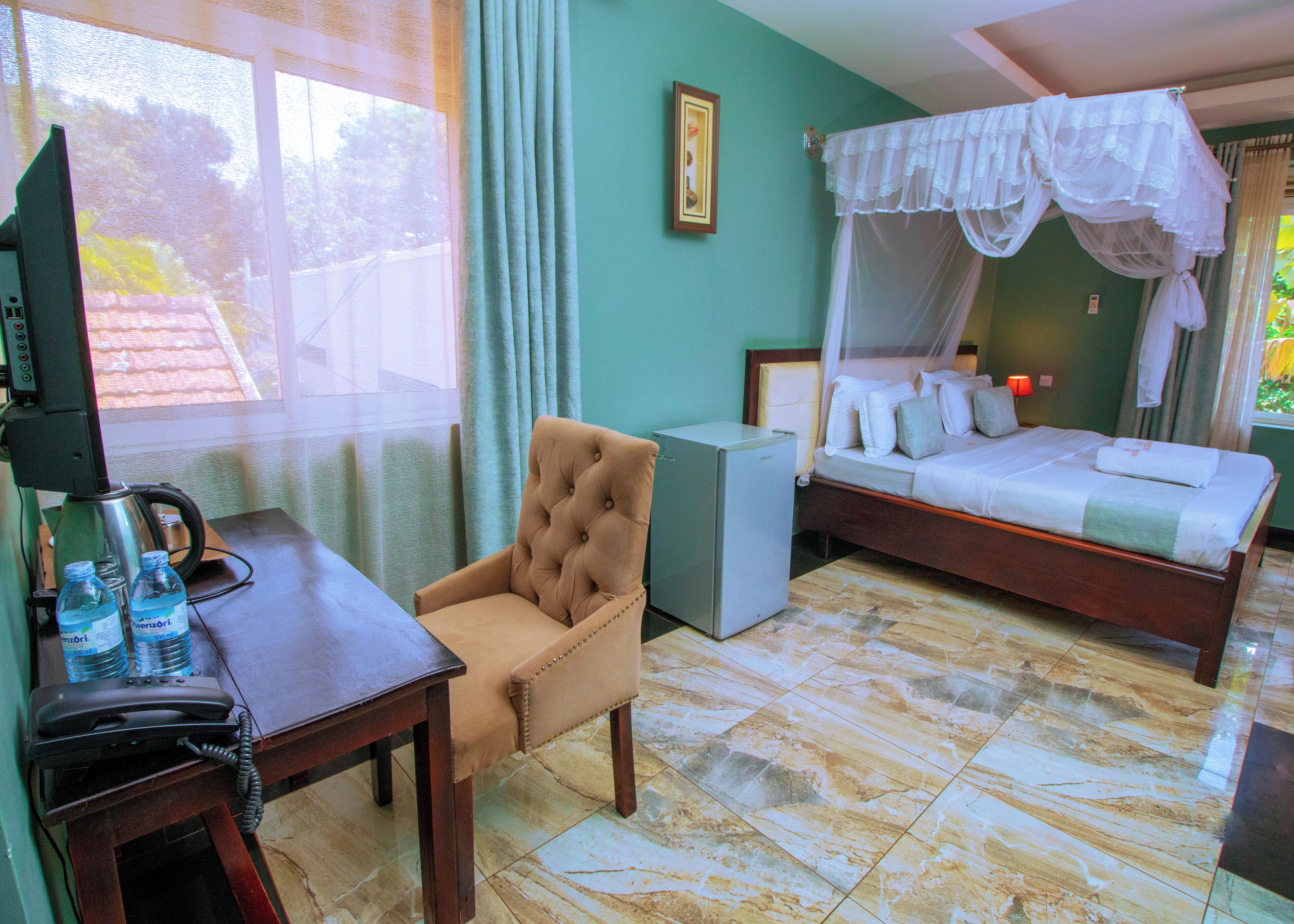 A hotel room with a bed, a chair, a desk with a telephone, and a small table with water bottles.