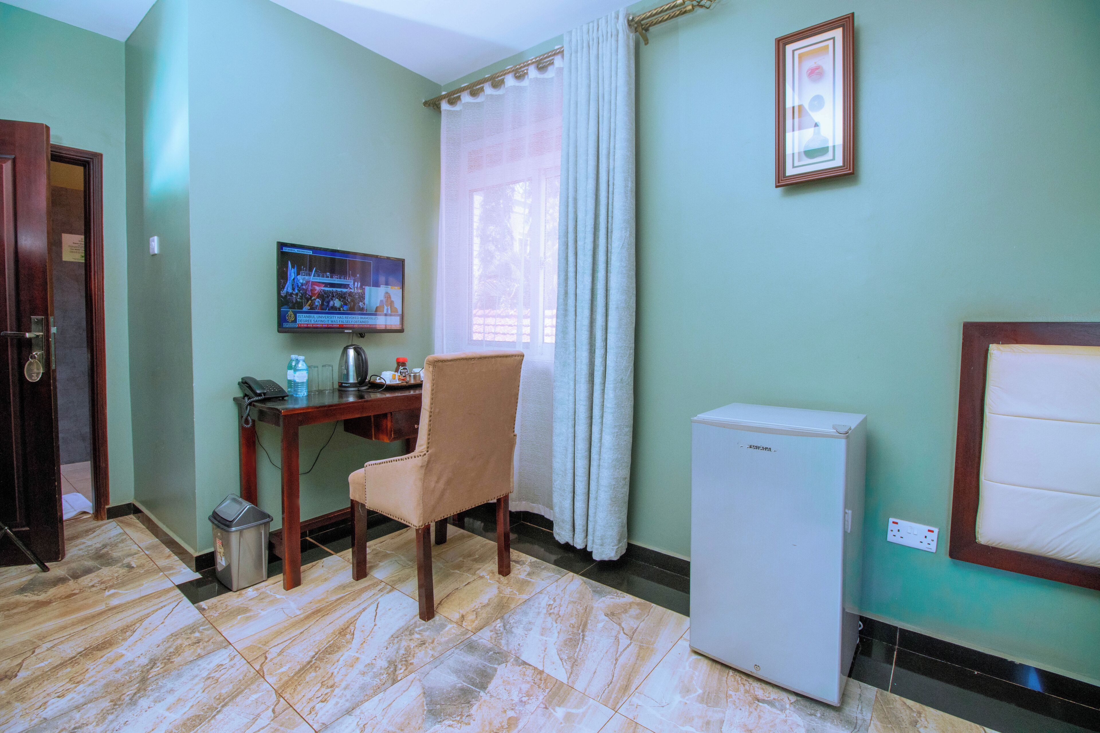 A room with a desk, chair, television, and a small refrigerator.