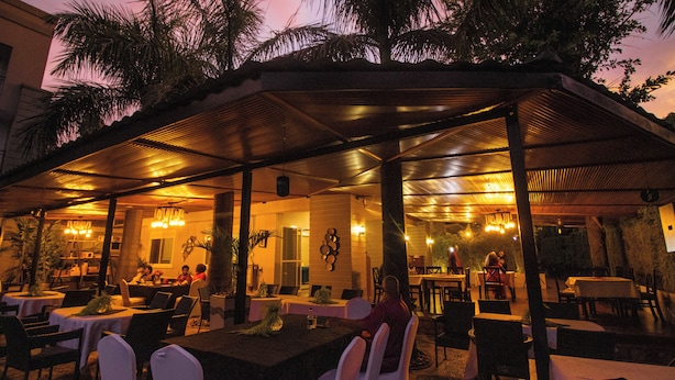 An outdoor dining area with tables and chairs, covered by a roof, and surrounded by palm trees. - The Mansion Hotel (Jinja)