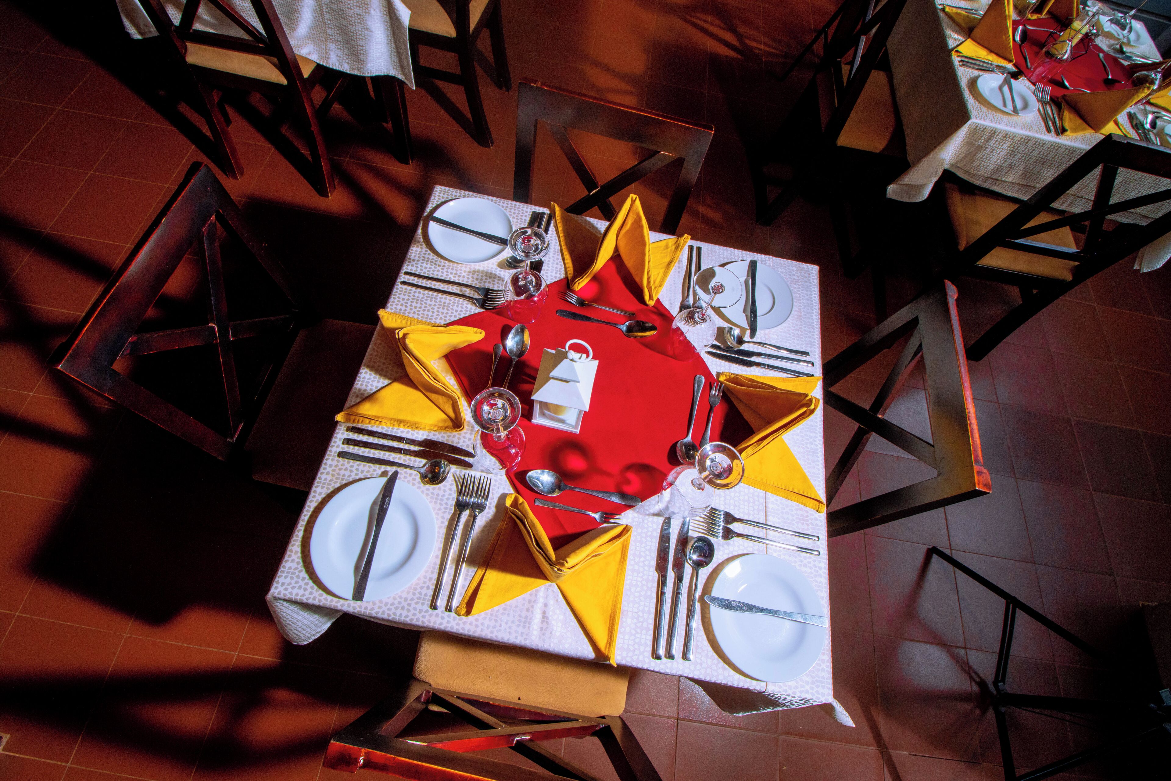 A dining table set with multiple chairs, each with a yellow napkin and a white tablecloth.
