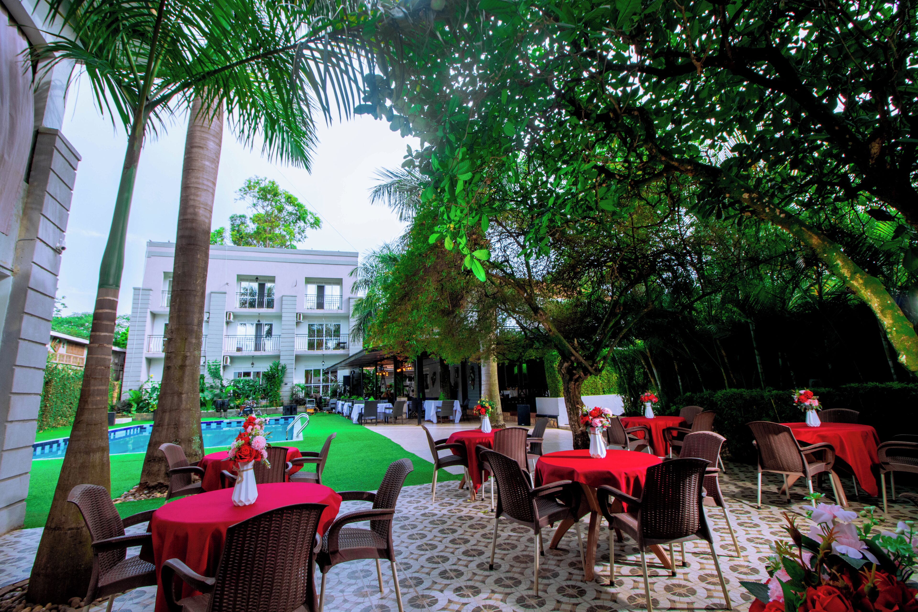 An outdoor dining area with tables and chairs, a pool in the background, and a building with balconies.