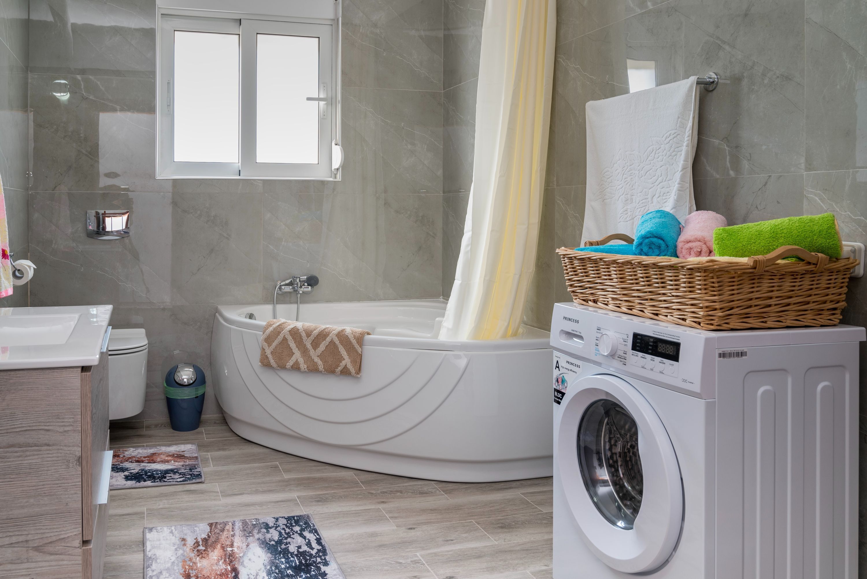 A modern bathroom with a built-in bathtub, a washing machine, and a wicker basket with towels.