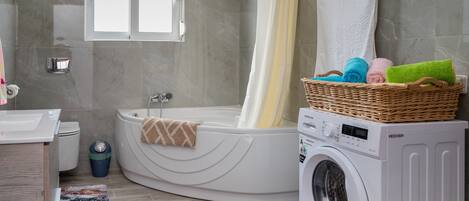 A modern bathroom with a built-in bathtub, a washing machine, and a wicker basket with towels.