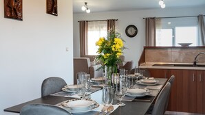 Spiseområde med et bord dækket til seks personer, en vase med gule blomster og et køkken i baggrunden.